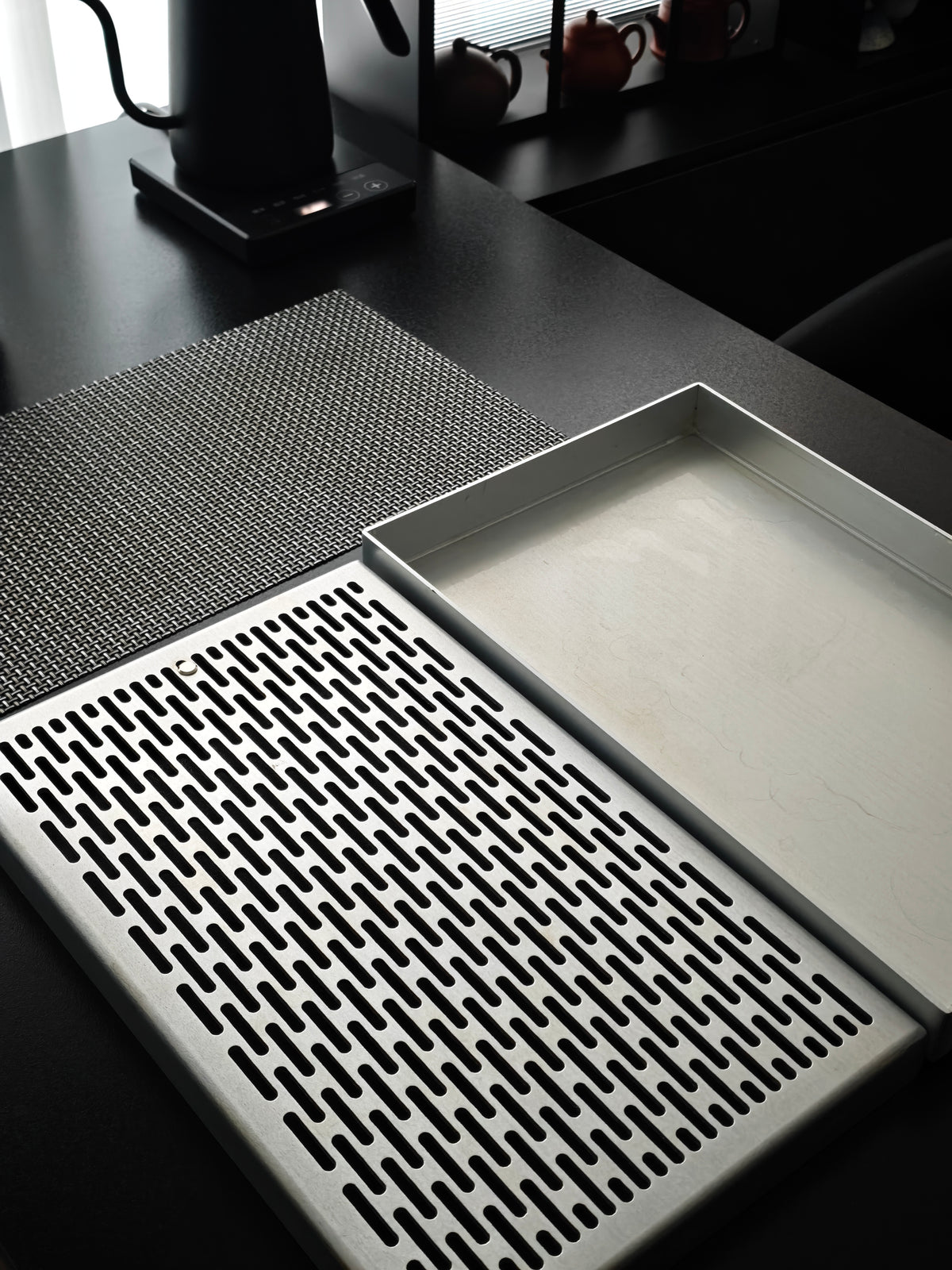 Tea tray and woven metal mat beside a kettle