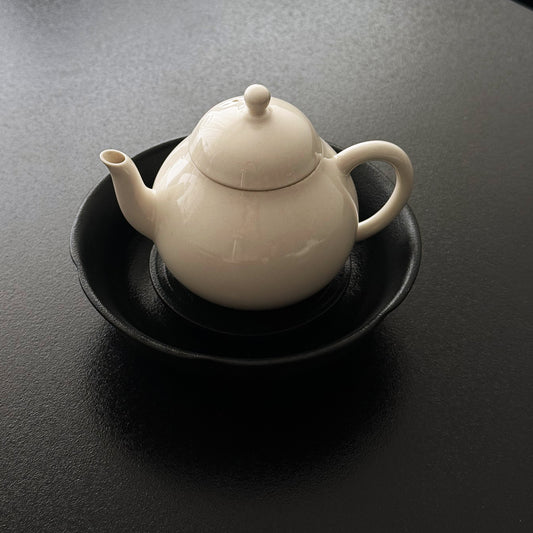 Ceramic teapot resting on a round black tray