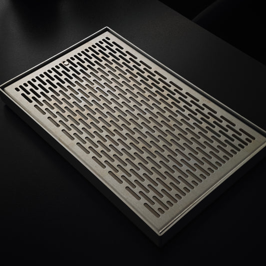 Rectangular slotted tea tray beside a woven metal mat