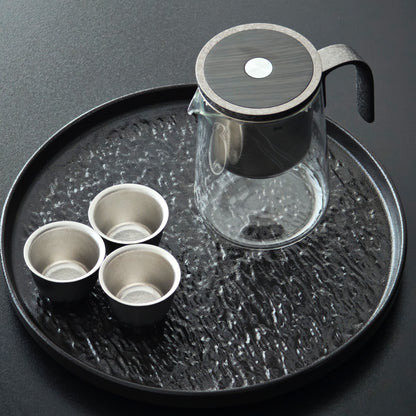 Tea brewer and three cups displayed on a round tray