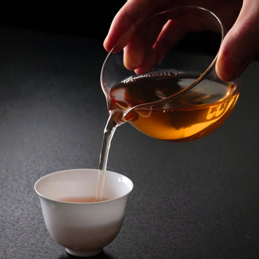 Tea being poured from the clear glass pitcher into a cup